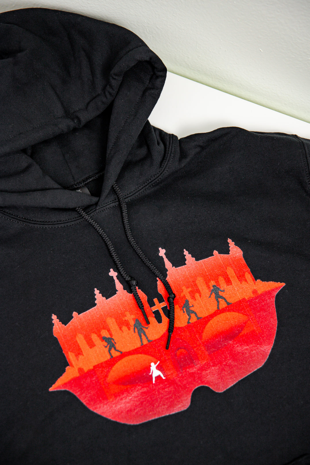 Black hoodie featuring red cityscape with shadowed figures and one white silhouette—SteamyBookworms exclusive merch.